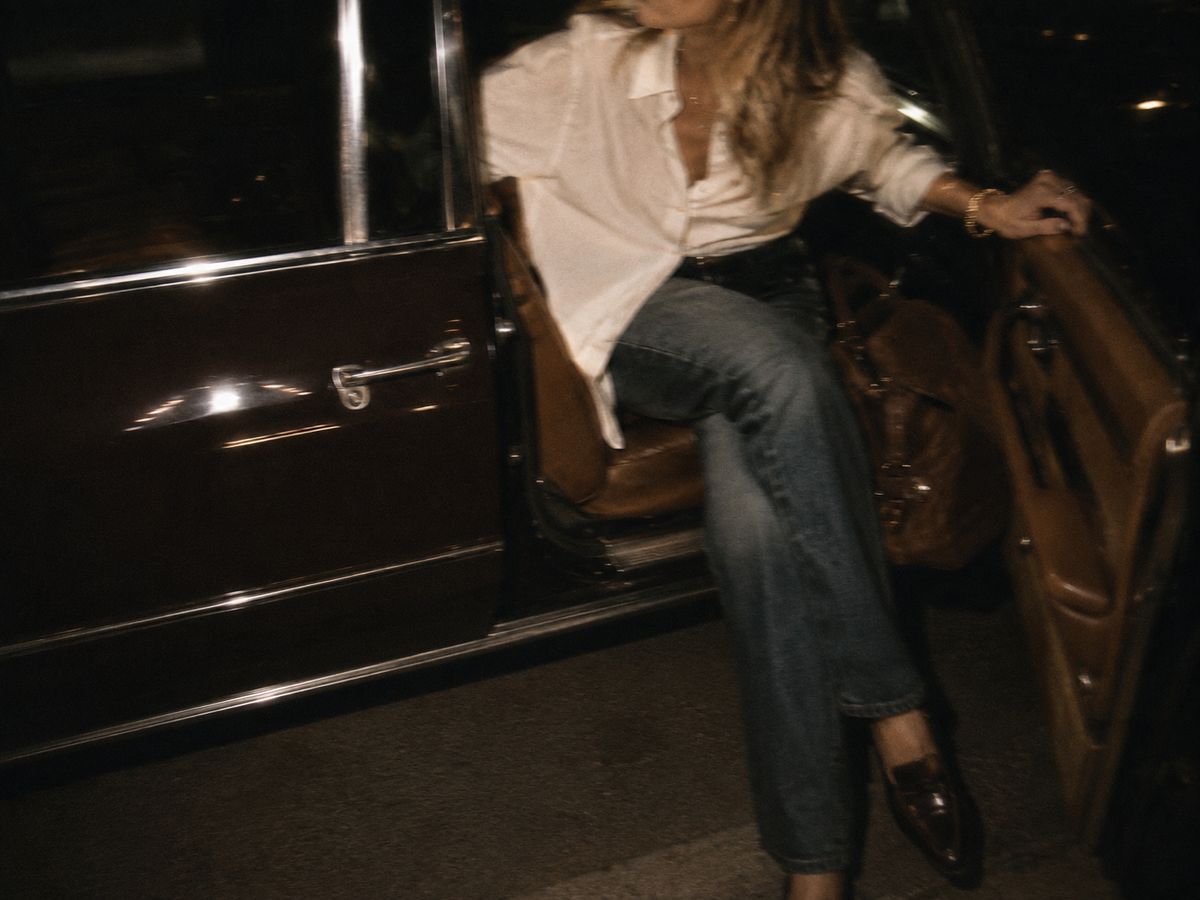 Woman in a white shirt and jeans stepping out of a vintage car at night
